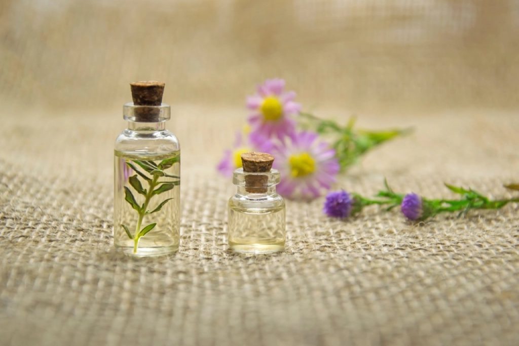 Due flaconi di vetro con erbe officinali e fiori viola sullo sfondo