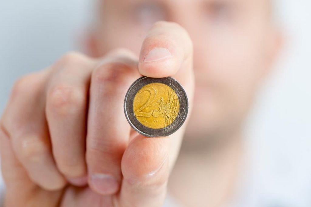 Mano che mostra una moneta da due euro, simbolo del prezzo dei farmaci galenici