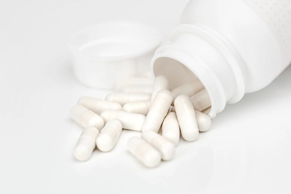 Capsule bianche uscite da un flacone bianco aperto